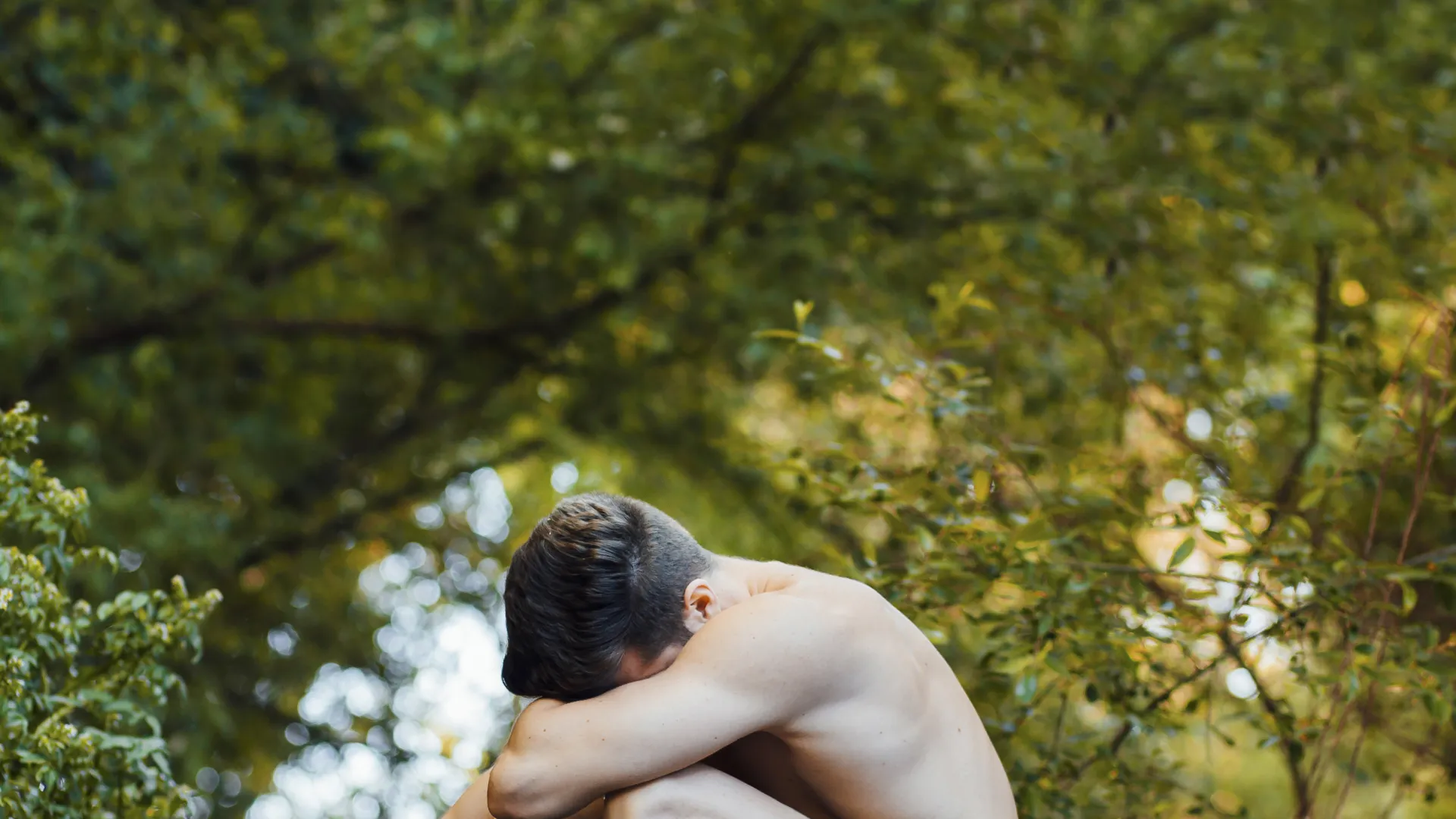 Uomo apparentemente nudo che piange nel giardino dell'eden, metafora di Adamo